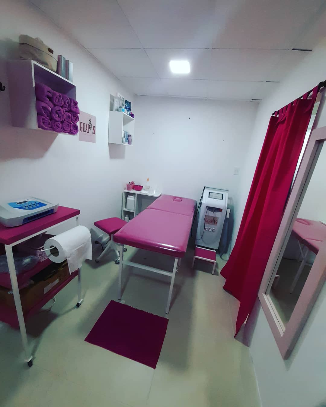Cabina de Guapas con camilla fucsia, toallas lilas, el equipo de electroestimulación y el láser CEC